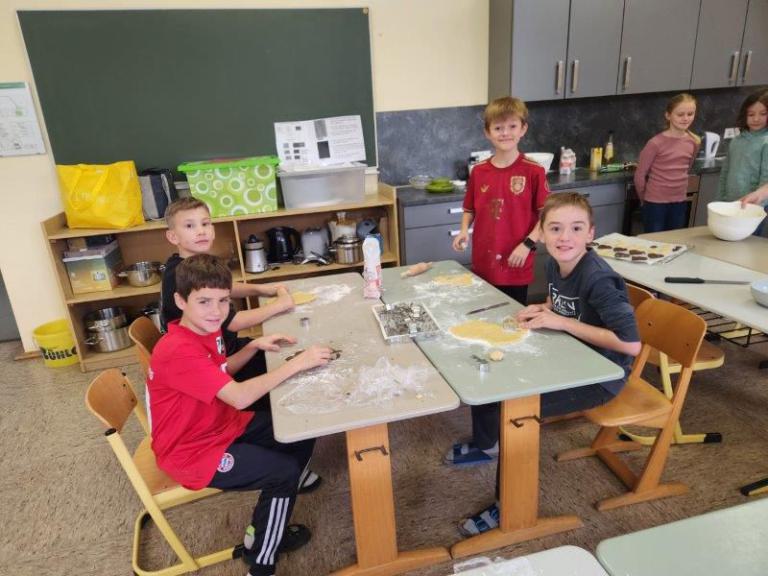 Kinder sitzen an zwei zusammengestellten Tischen und kneten Teig, auf den Tischen liegen Backutensilien und Teigreste.