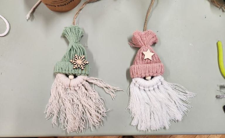 Zwei handgefertigte Wichtelanhänger mit langen, weißen Bärten, einer mit grünem, der andere mit rosafarbenem Mützchen, verziert mit Holzornamenten.