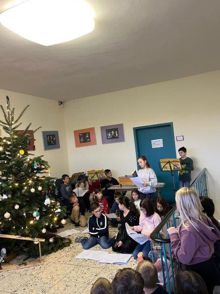 Gruppe von Kindern sitzt und steht vor einem geschmücktem Weihnachtsbaum