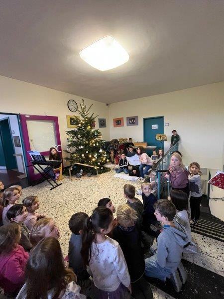 Kinder sitzen und stehen vor einem geschmückten Weihnachtsbaum und einem Keyboard an der Wand.
