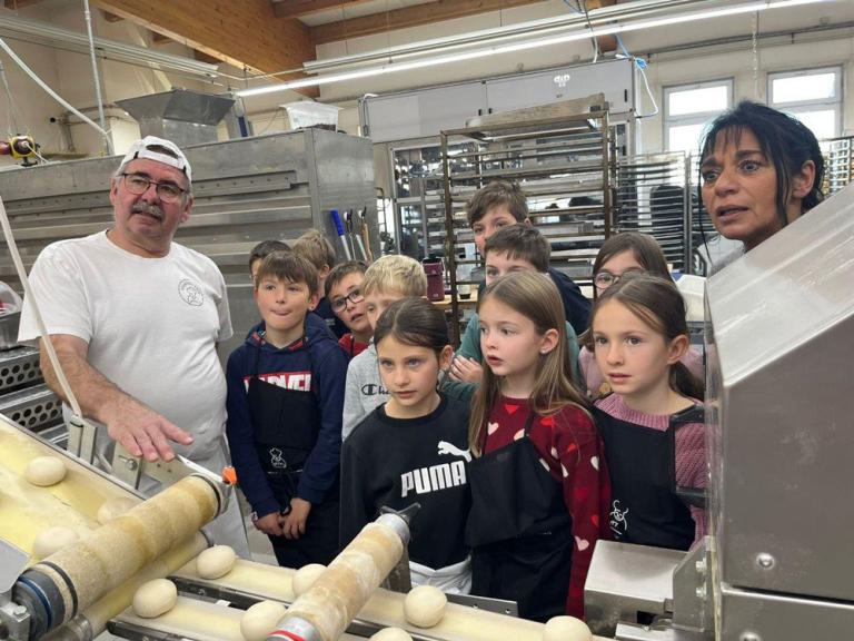 Eine Gruppe von Kindern lässt sich eine Backmaschine von einem Bäcker erklären
