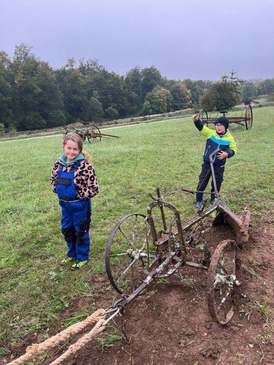 Zwei Kinder stehen bei einem alten Pflug auf dem Acker