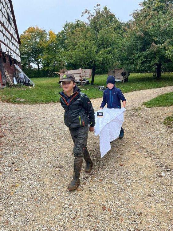 Zwei Kinder tragen ein mit weißer Decke bedecktes Brett auf einem Kiesweg