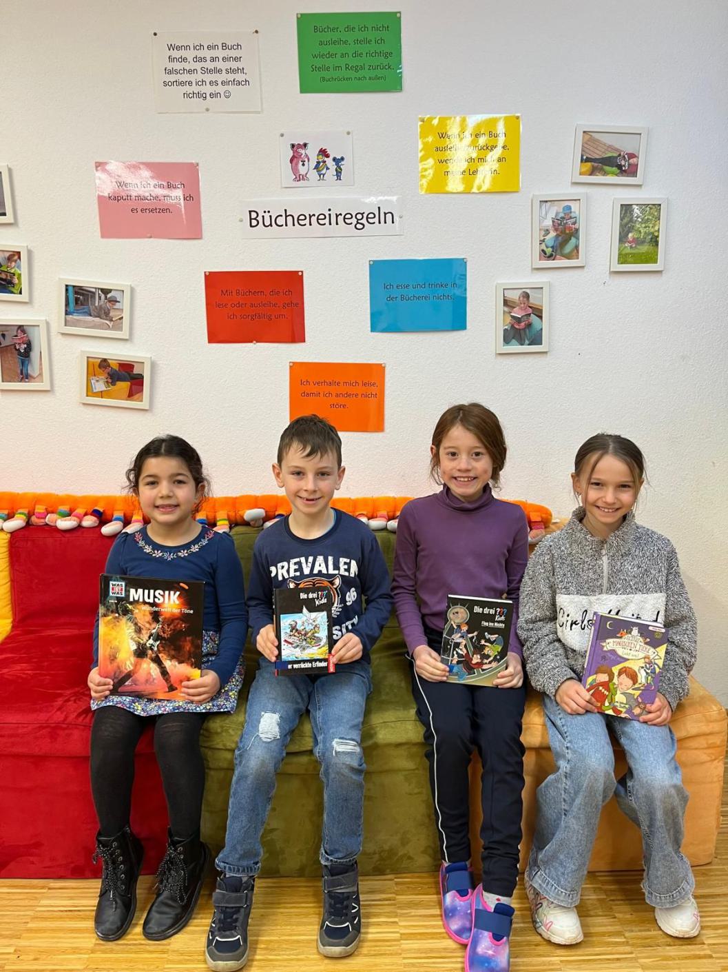 Vier Kinder sitzen auf einem Sofa und präsentieren ihr Bücher