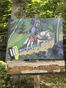 Historische Szene mit Ritter und Pferd vor einem Burggemälde, darunter ein Holzschild mit dem Namen zur Burg Falkenstein.