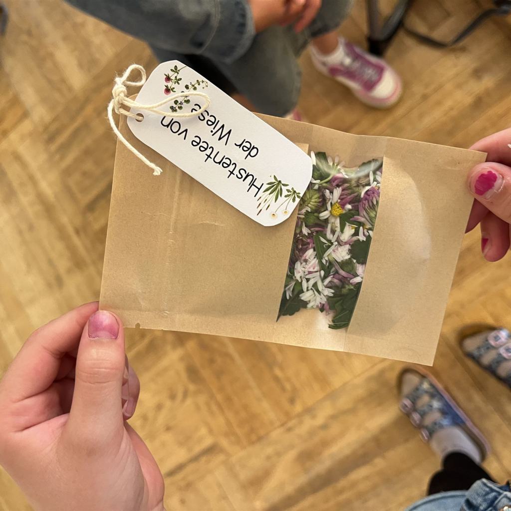 Eine Person hält ein Päckchen mit dem Aufdruck Hustentee der Wiese, das Blumenmuster trägt.