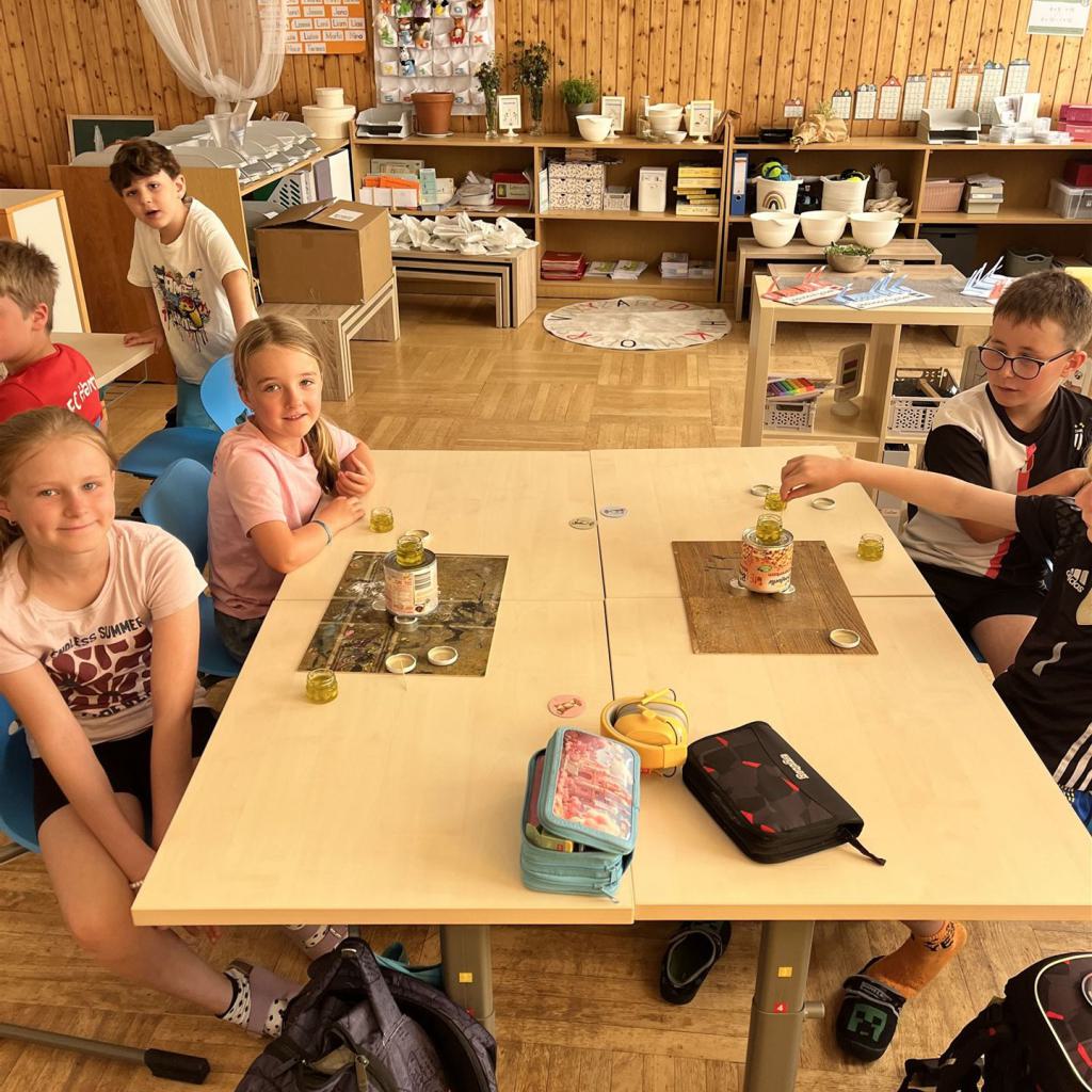 Kinder in einem Klassenzimmer, umgeben von Regalen voller Materialien.