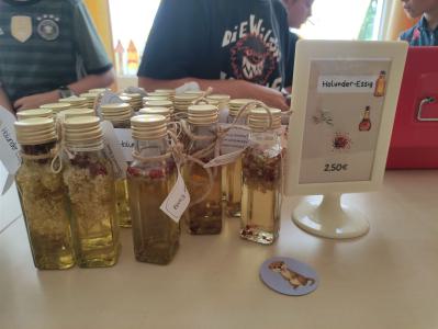 Eine Reihe von kleinen Glasflaschen mit Flüssigkeiten, darunter Holunder-Essig, sind auf einem Tisch zum Verkauf ausgestellt.