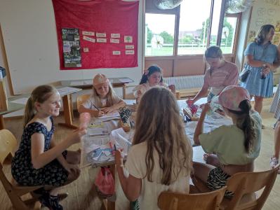 Eine Gruppe von Menschen sitzt an Tischen in einem hell beleuchteten Raum, der für einen Kurs oder ein Treffen genutzt wird.